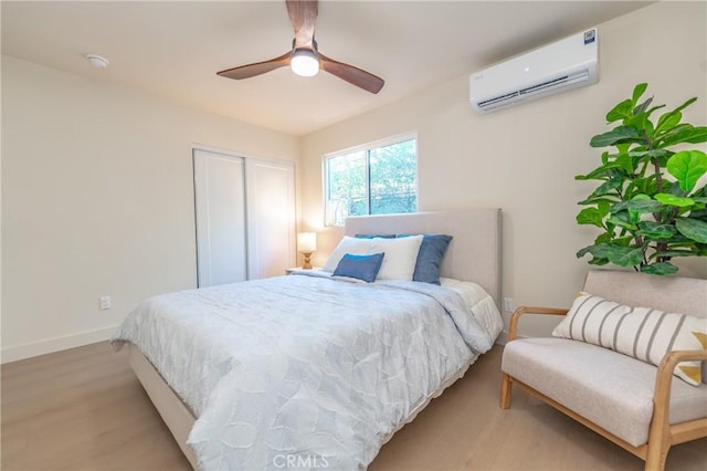 bedroom with light wood-type flooring, an AC wall unit, ceiling fan, and a closet