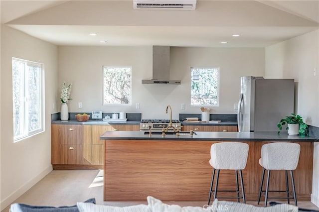 kitchen featuring sink, wall chimney exhaust hood, a kitchen breakfast bar, stainless steel refrigerator, and a wall mounted air conditioner