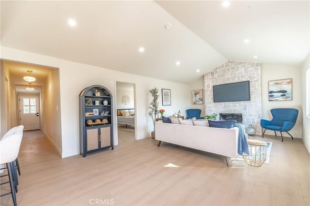 living room featuring a stone fireplace, vaulted ceiling, built in features, and light hardwood / wood-style flooring