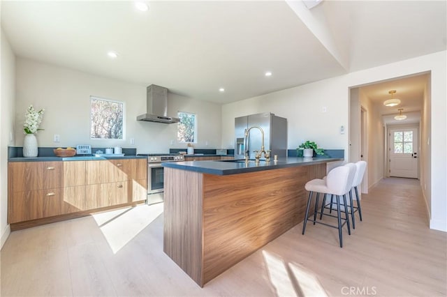 kitchen with wall chimney exhaust hood, stainless steel appliances, light wood-type flooring, a kitchen breakfast bar, and sink