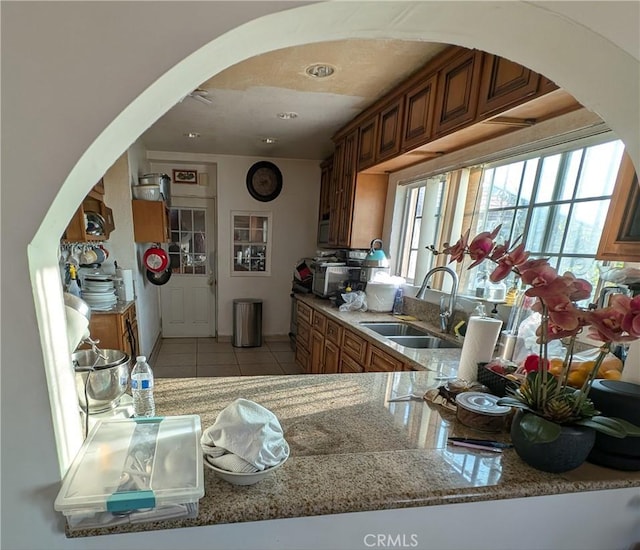 kitchen with light stone countertops, sink, kitchen peninsula, and light tile patterned flooring