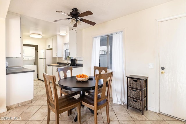 dining space featuring ceiling fan, sink, stacked washer and dryer, and light tile patterned flooring