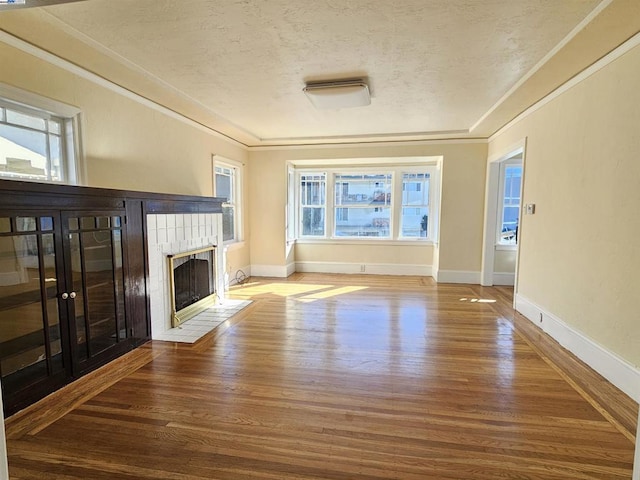 unfurnished living room with a textured ceiling, a tiled fireplace, hardwood / wood-style flooring, and a healthy amount of sunlight