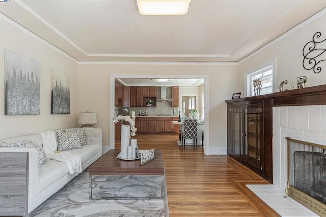 living room featuring a tile fireplace, ornamental molding, and hardwood / wood-style flooring