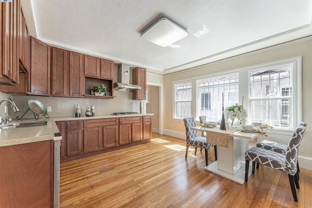 kitchen featuring light hardwood / wood-style floors, stainless steel gas cooktop, sink, wall chimney range hood, and backsplash