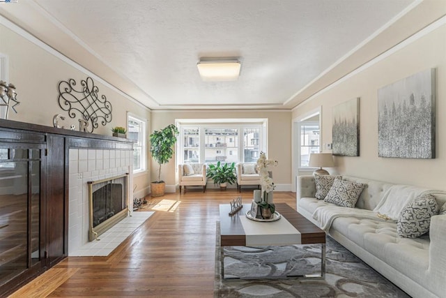 living room featuring a tile fireplace, hardwood / wood-style floors, a wealth of natural light, and ornamental molding