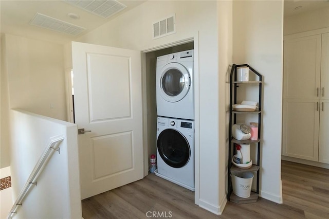 clothes washing area with stacked washing maching and dryer, wood finished floors, and visible vents