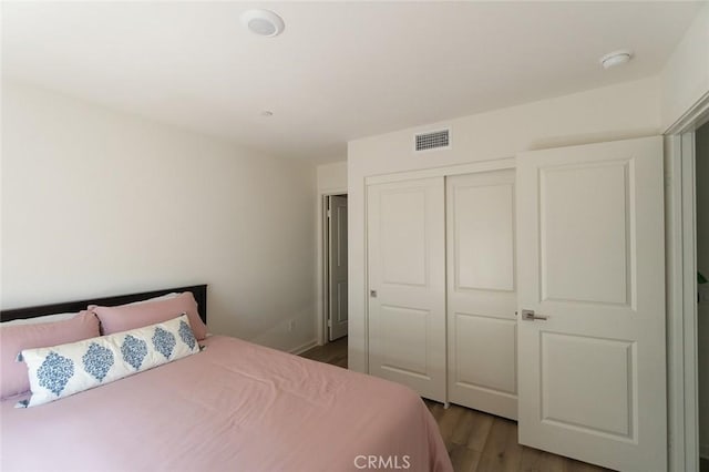 bedroom with wood finished floors, visible vents, and a closet