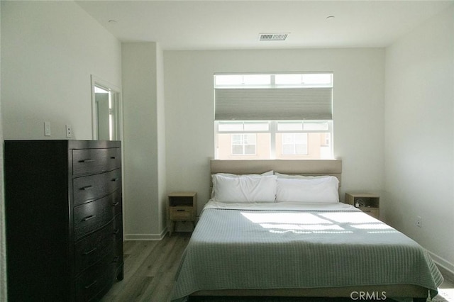 bedroom with baseboards, visible vents, and wood finished floors