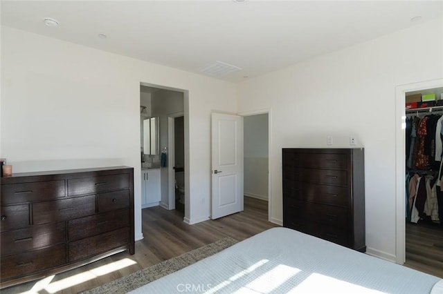 bedroom featuring connected bathroom, a walk in closet, a closet, and dark hardwood / wood-style flooring