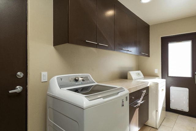 clothes washing area featuring light tile patterned flooring, washer and dryer, and cabinets