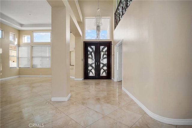 foyer entrance with an inviting chandelier, a towering ceiling, and french doors