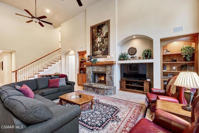 living room featuring high vaulted ceiling, ceiling fan, built in features, and a stone fireplace