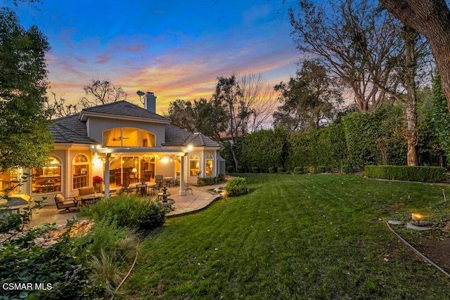 back house at dusk with a lawn, ceiling fan, a patio area, and an outdoor living space