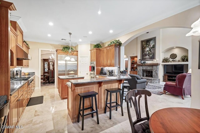 kitchen with decorative light fixtures, a fireplace, stone counters, a kitchen bar, and appliances with stainless steel finishes