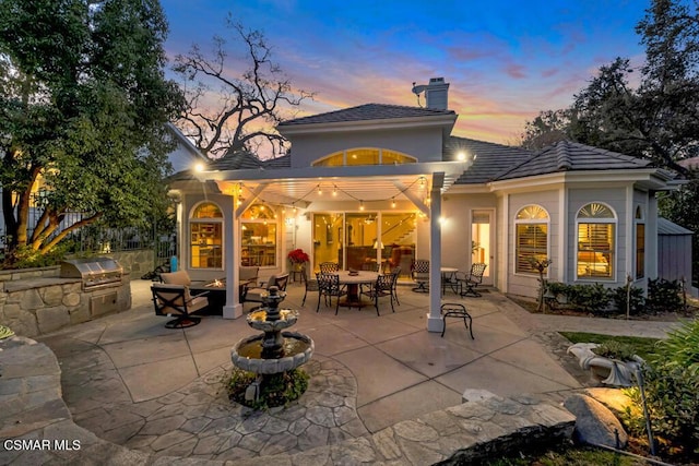 back house at dusk with exterior kitchen and a patio area