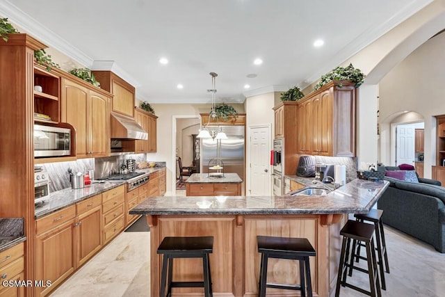 kitchen with kitchen peninsula, built in appliances, crown molding, a breakfast bar, and sink