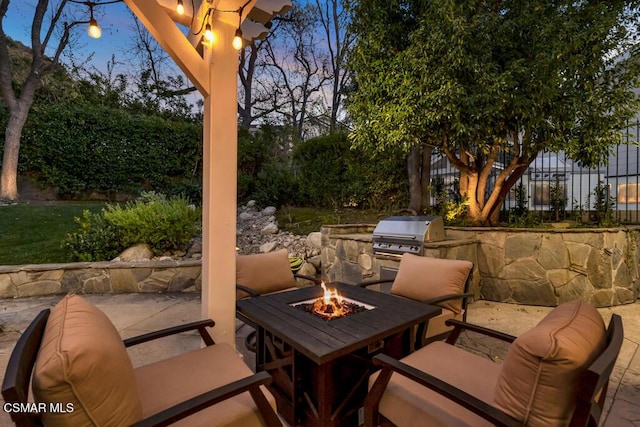 patio terrace at dusk with exterior kitchen, an outdoor fire pit, and grilling area