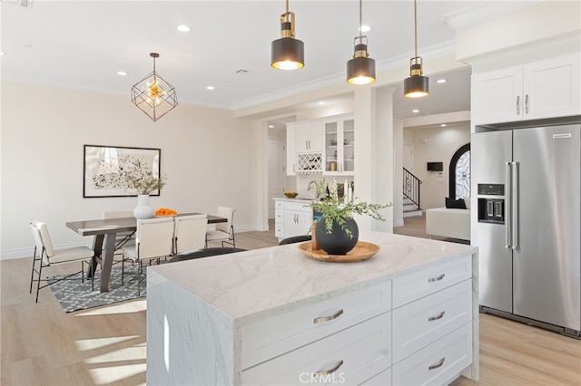 kitchen featuring light stone counters, hanging light fixtures, a kitchen island, white cabinetry, and high quality fridge