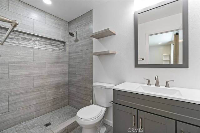 bathroom with toilet, a tile shower, and vanity