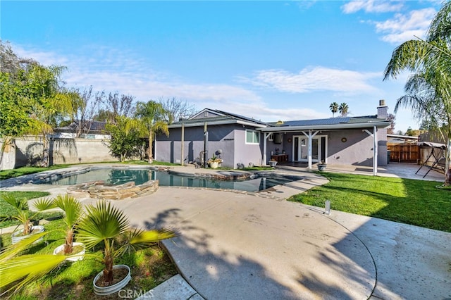 back of property with a fenced in pool, a patio area, a yard, and solar panels