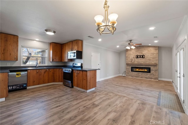 kitchen with pendant lighting, appliances with stainless steel finishes, sink, a large fireplace, and light hardwood / wood-style flooring