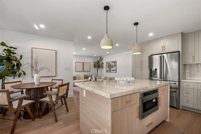 kitchen with light stone countertops, hanging light fixtures, a center island, light hardwood / wood-style floors, and appliances with stainless steel finishes