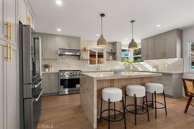 kitchen with high end appliances, a center island, gray cabinets, wood-type flooring, and sink