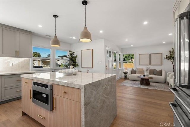 kitchen with gray cabinetry, decorative backsplash, light stone countertops, and a kitchen island