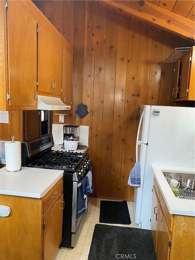 kitchen with sink, wooden walls, light tile patterned floors, gas range, and white refrigerator