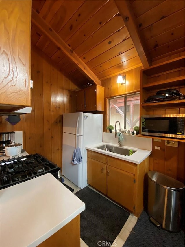 kitchen featuring sink, white refrigerator, beamed ceiling, and wooden walls