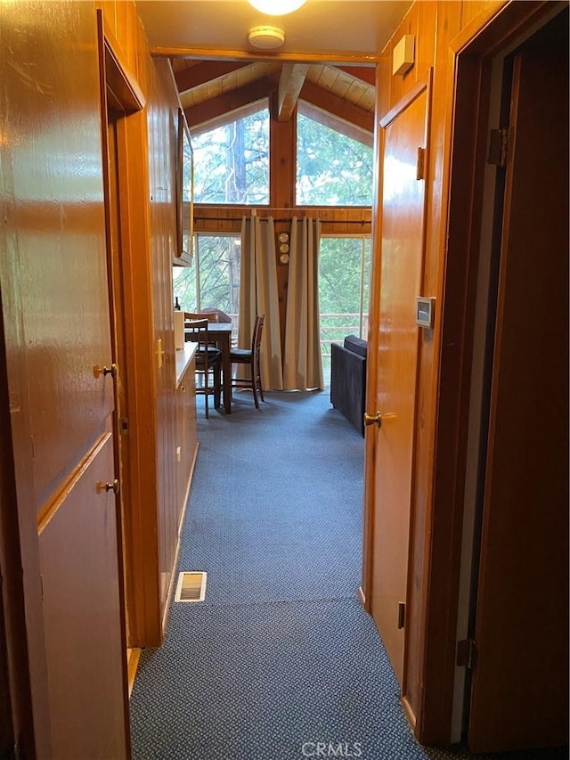 hall featuring dark carpet, lofted ceiling, and wooden walls