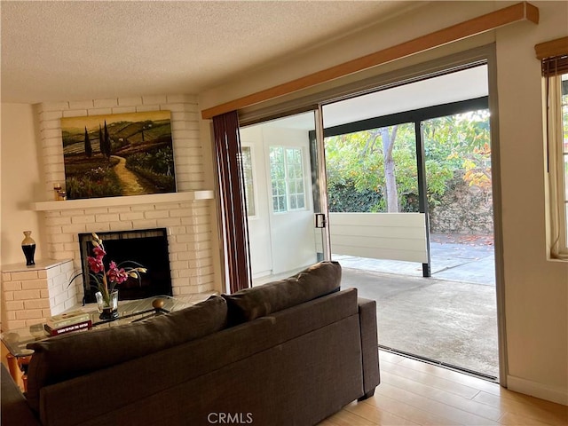 living room featuring a textured ceiling, a brick fireplace, and light hardwood / wood-style flooring