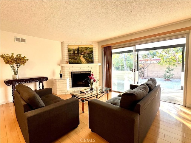 living room featuring a brick fireplace, a textured ceiling, and light hardwood / wood-style flooring