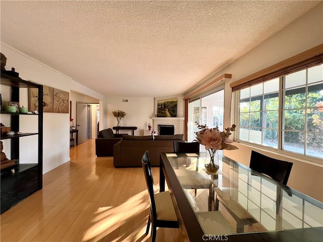 dining room with a textured ceiling, a brick fireplace, and light hardwood / wood-style floors