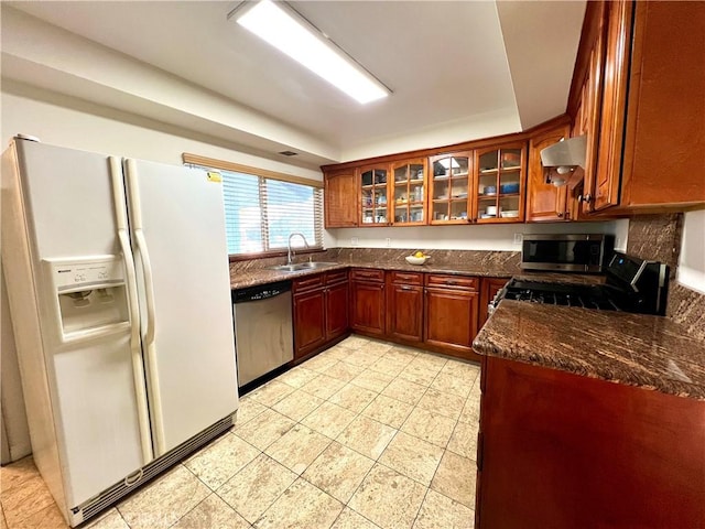 kitchen featuring appliances with stainless steel finishes, wall chimney range hood, dark stone counters, and sink