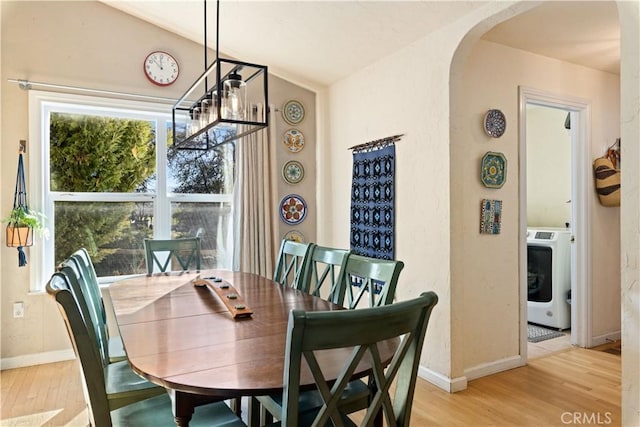 dining space with light wood-type flooring, lofted ceiling, a chandelier, and washer / clothes dryer