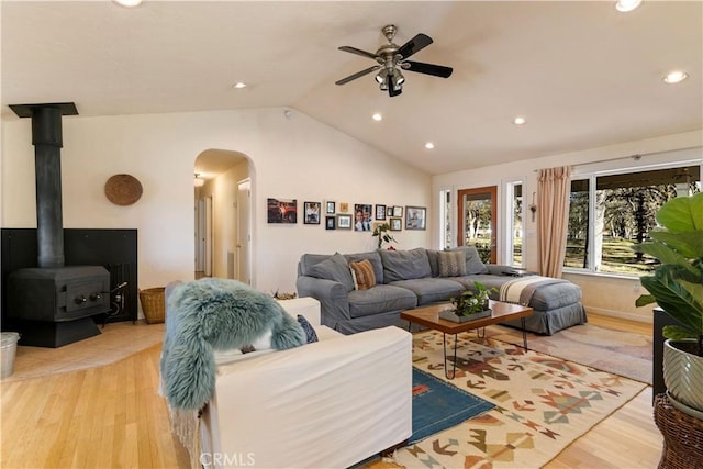 living room featuring ceiling fan, a wood stove, vaulted ceiling, and light wood-type flooring