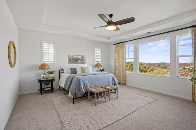 carpeted bedroom featuring ceiling fan, multiple windows, and a tray ceiling