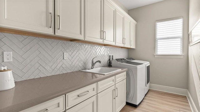 clothes washing area with cabinets, sink, independent washer and dryer, and light hardwood / wood-style floors