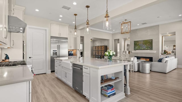 kitchen with white cabinetry, an island with sink, hanging light fixtures, and exhaust hood