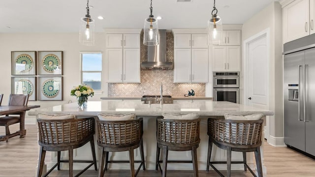 kitchen with wall chimney exhaust hood, stainless steel appliances, and an island with sink