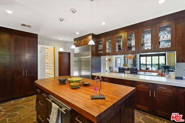 kitchen featuring light stone counters, decorative light fixtures, a center island, stainless steel built in fridge, and kitchen peninsula