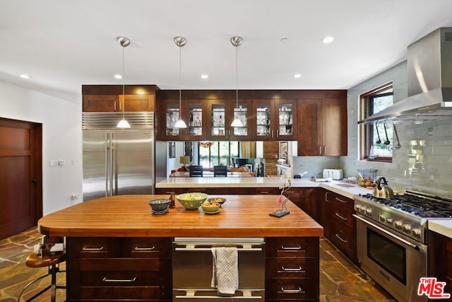 kitchen with wall chimney range hood, high end appliances, tasteful backsplash, decorative light fixtures, and kitchen peninsula