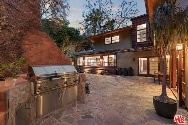 patio terrace at dusk featuring an outdoor kitchen and a grill