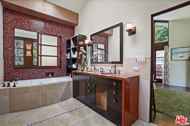 bathroom featuring a relaxing tiled tub, tile patterned floors, vanity, and tile walls