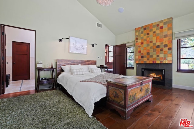 bedroom with a tile fireplace, dark wood-type flooring, and high vaulted ceiling