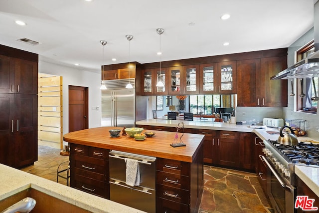 kitchen featuring tasteful backsplash, high end appliances, wall chimney range hood, and decorative light fixtures