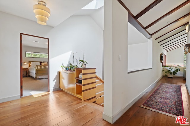 corridor with vaulted ceiling with skylight and hardwood / wood-style floors