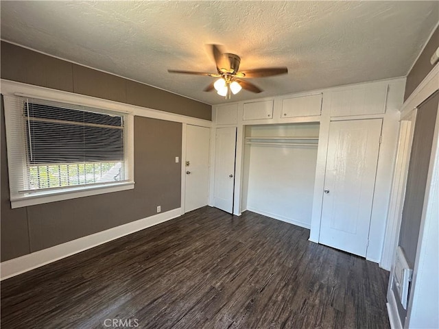 unfurnished bedroom with ceiling fan, a textured ceiling, dark hardwood / wood-style floors, and multiple closets